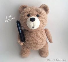 a crocheted teddy bear with a cell phone in it's hand, on a white background