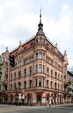 an old building on the corner of a street with traffic lights and people walking by