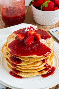 a stack of pancakes covered in syrup and topped with strawberries on a white plate