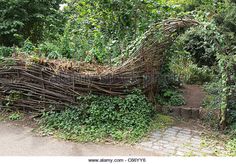 a sculpture made out of branches and vines in the middle of a park, surrounded by greenery