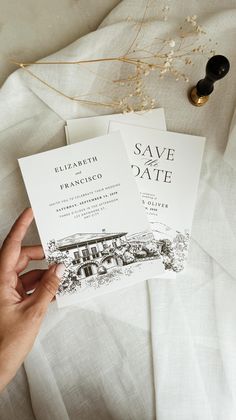 someone holding two save the date cards on top of a white sheet with flowers in it