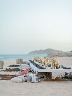 a long table set up on the beach for an outdoor dinner with candles and flowers