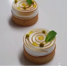 two small desserts with white frosting and green leaves on top, sitting on a table