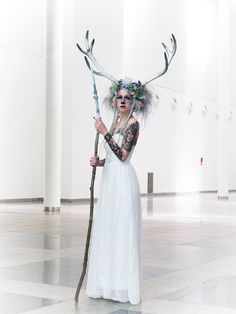 a woman in a white dress holding a stick and wearing antlers on her head