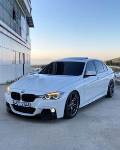 a white bmw car parked in front of a building with the sun shining on it