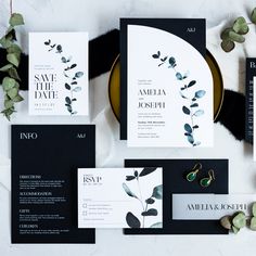 the wedding stationery is laid out on a table with greenery and black paper