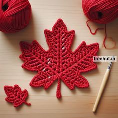 red crocheted leaf next to ball of yarn and knitting needle on wooden table