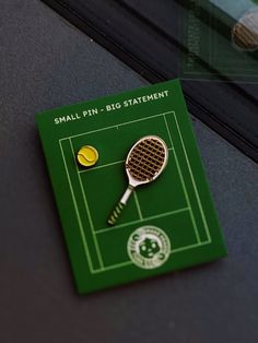 a tennis racket and ball pin sitting on top of a green brochure