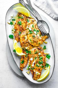 grilled chicken with lemon and parsley on a white plate next to a fork