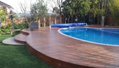 a wooden deck next to a swimming pool in a backyard with green grass and trees