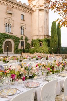 an outdoor dining area with white chairs and tables set up for a formal dinner in front of a castle