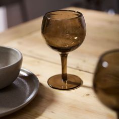 a wine glass sitting on top of a wooden table next to a bowl and saucer