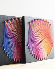 two pieces of art that are sitting on a table next to each other, one is made out of wood and the other has multicolored paper