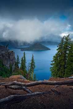 a large body of water surrounded by trees on a cloudy day with dark clouds in the sky