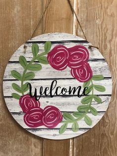 a welcome sign hanging on the side of a wooden door with flowers painted on it