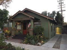 a small green house with an american flag on the front door and landscaping around it