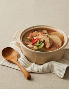 a bowl of soup with meat and vegetables in it on a white cloth next to a wooden spoon