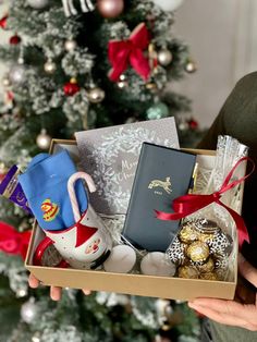 someone is holding a christmas gift box in front of a tree