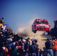 a red rally car driving down a dirt road with people watching from the sidelines