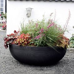 a large planter filled with lots of flowers next to a white wall and building