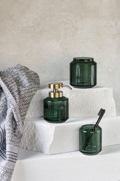 three green glass jars sitting on top of a white shelf next to a towel and toothbrush