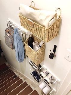 two wicker baskets hanging on the wall with clothes and shoes in them next to a coat rack