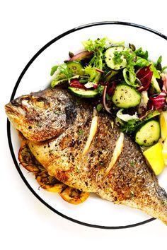 a white plate topped with fish next to a salad