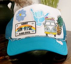 Turquoise and white custom beachy trucker hat. Multiple beach theme patches with silver chain detail. Mesh back hat with adjustable snap band. Blue Adjustable Summer Trucker Hat, Blue Adjustable Trucker Hat For Summer, White Trucker Hat For The Beach, Fun Blue Trucker Hat For Vacation, Adjustable Blue Trucker Hat For Beach, Bohemian Beach Trucker Hat, Blue Trucker Snapback Hat For Beach, Blue Snapback Trucker Hat For Festival, Bohemian Adjustable Trucker Hat For Beach