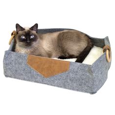 a siamese cat is sitting in a gray felt bed with leather trimmings