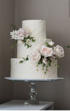 three tiered white wedding cake with pink roses on the side and greenery on top