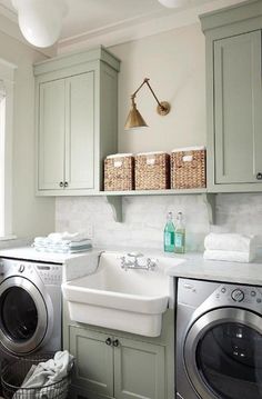 a washer and dryer in a small room with green cabinets, white counter tops and gray flooring