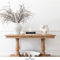 a table with vases and books on it next to a white planter filled with branches