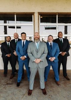 a group of men standing next to each other wearing suits and ties with their hands in their pockets