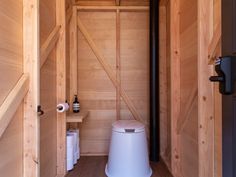 there is a toilet in the bathroom with wooden walls and doors on both sides, next to a trash can