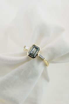 an emerald and diamond ring sitting on top of a white cloth with a gold band