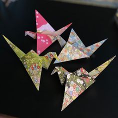 four origami birds sitting on top of a black table next to each other