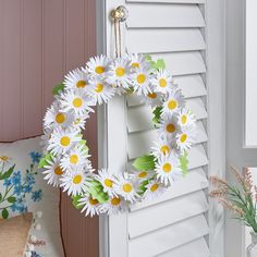 a wreath with daisies hanging from the side of a door next to a window