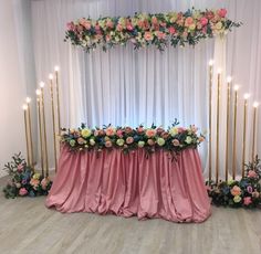 an arrangement of flowers and candles on a table with pink cloth draped over the top