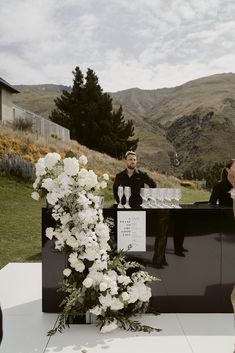 a man standing behind a black counter with white flowers on it next to a woman