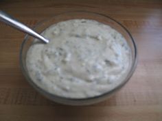 a glass bowl filled with white sauce on top of a wooden table