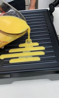 a person pouring orange juice on top of an electric grill with yellow spatulas