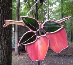 a pink stained glass flower hanging from a chain in the woods with trees behind it