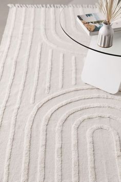 a white rug on top of a glass table with a book and vase in the background