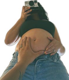 a pregnant woman taking a selfie with her camera in the shape of a belly