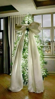 a white christmas tree with lights in the corner and ribbon on it's top