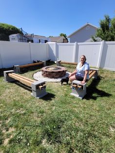 a woman sitting on a bench next to a fire pit in the grass near a fence