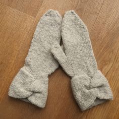 two gray mittens with bows on them sitting on a wooden floor