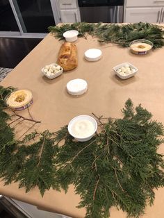 a table topped with bowls and plates covered in greenery next to a loaf of bread