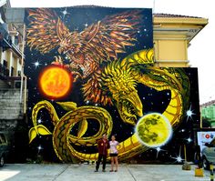 two people standing in front of a large mural on the side of a building,