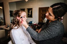 a woman is getting her make up done by another woman in a room with other people